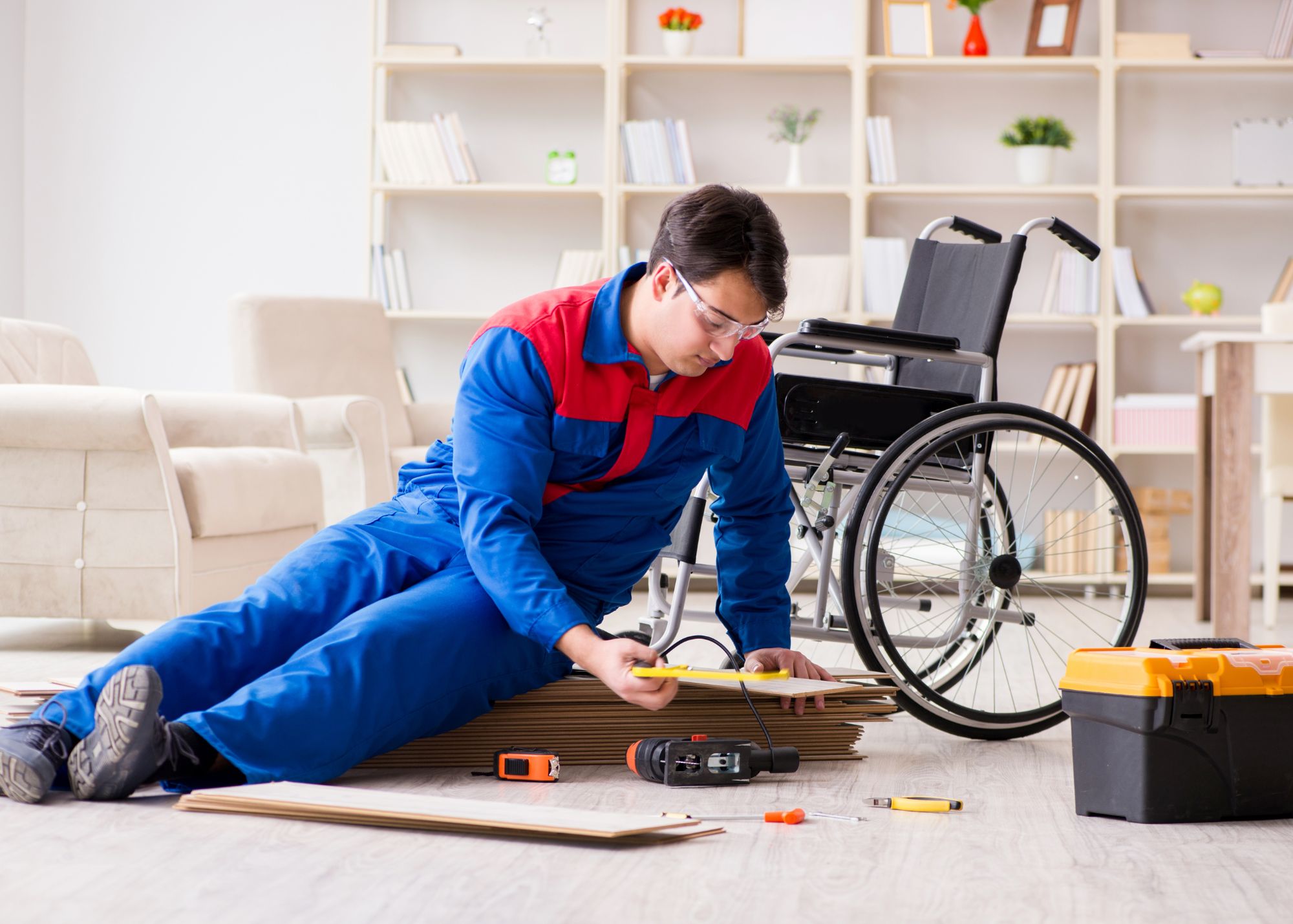 A man in a wheelchair is focused on working on the floor, surrounded by tools and materials.